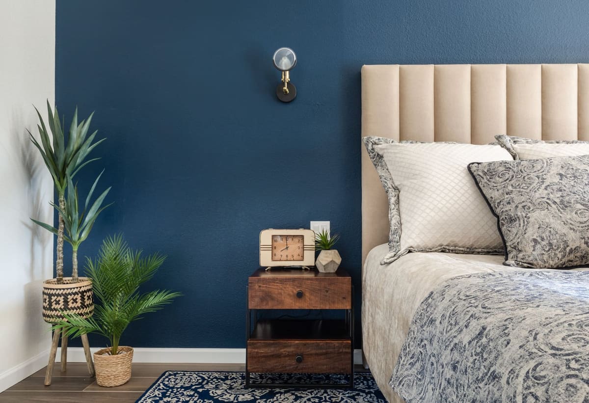 Cream channel headboard against a navy accent wall with a wood nightstand and potted palms
