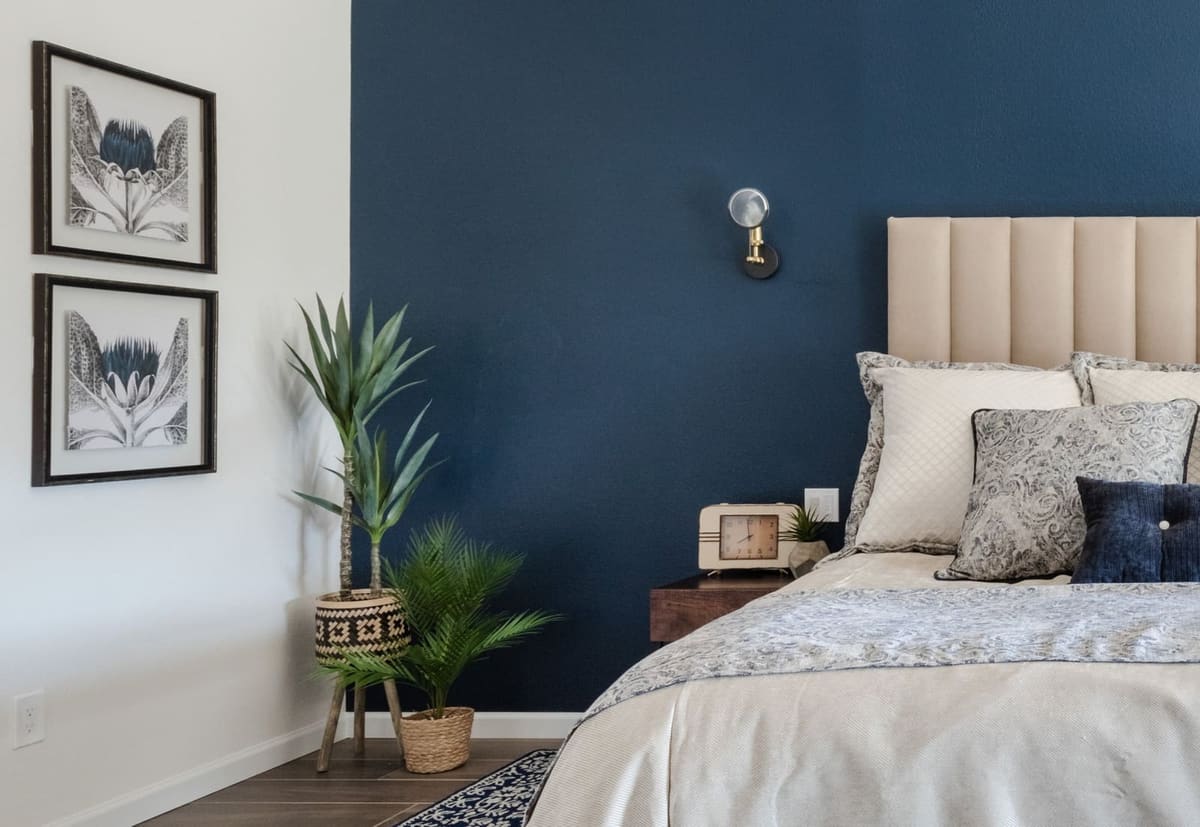 Navy accent wall with framed botanical prints, potted palms and a cream channel headboard