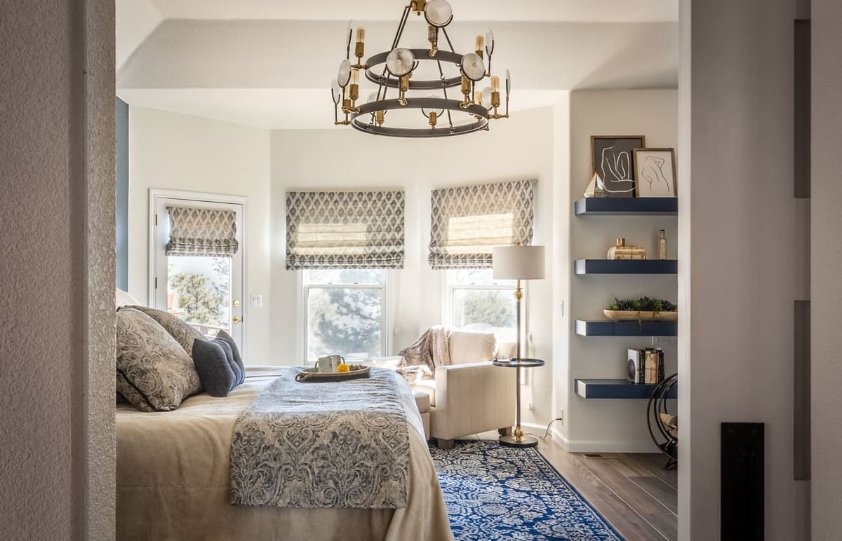 Bedroom bay window with patterned Roman shades seen past the bed, navy shelves on the right