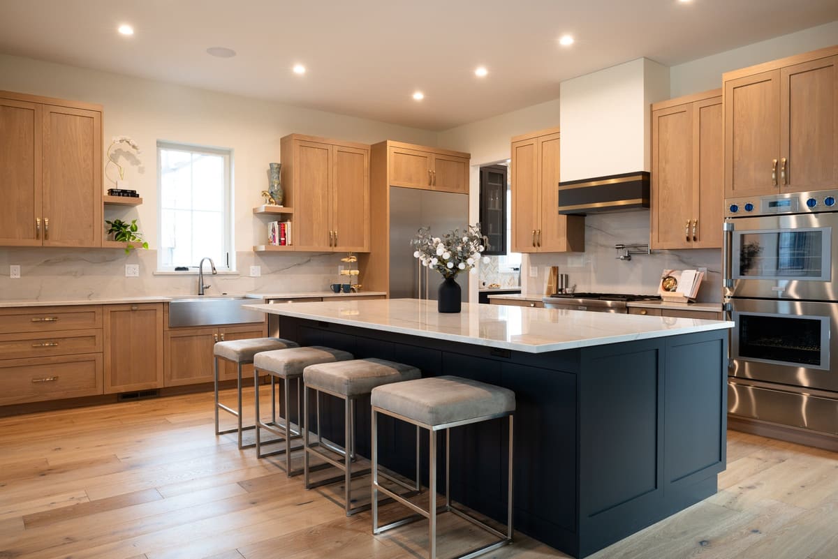 Kitchen remodel with white oak shaker cabinets, a navy island with upholstered stools and a white plaster range hood