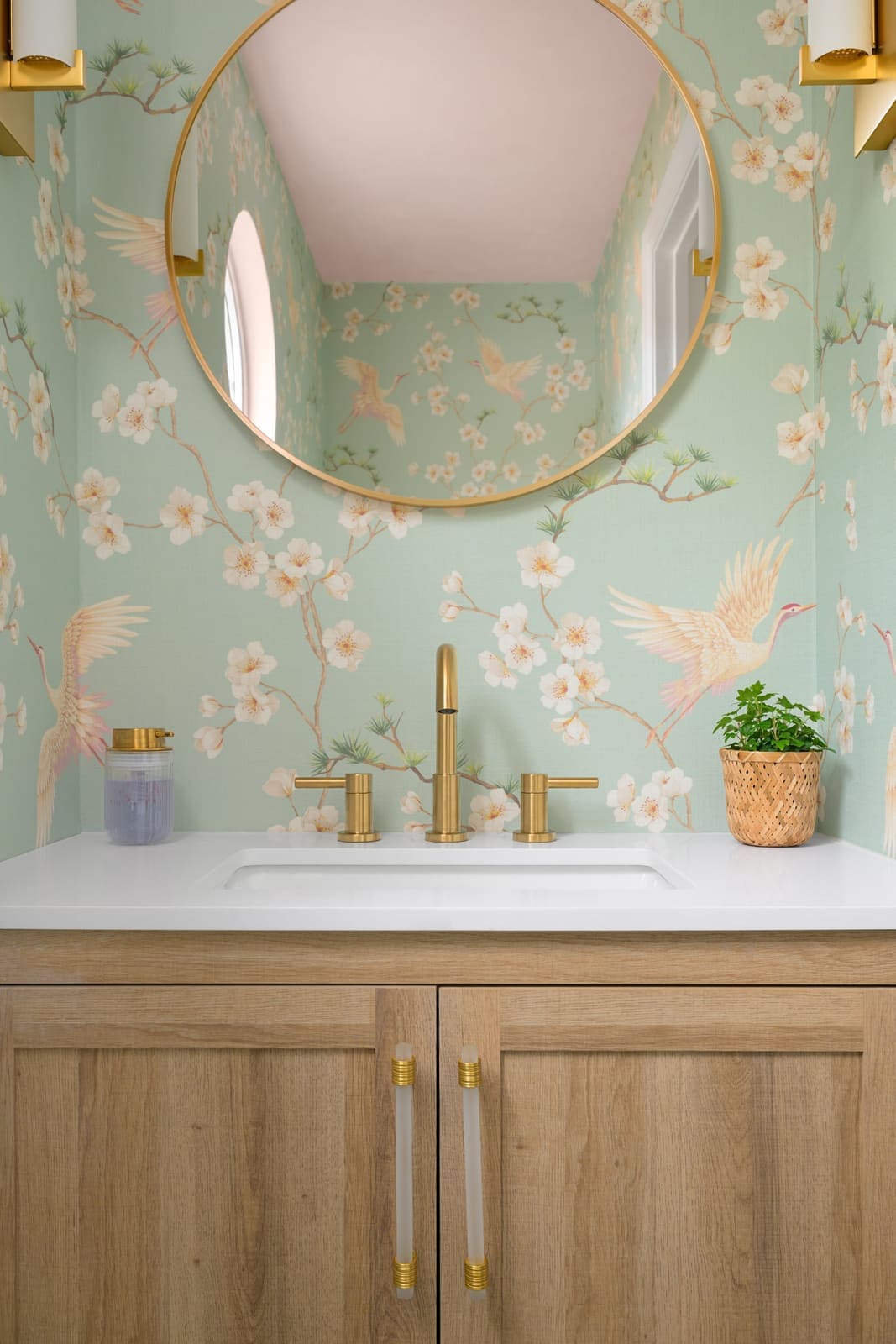 Powder room vanity in light oak with brass pulls, a brushed gold faucet and mint chinoiserie crane wallpaper