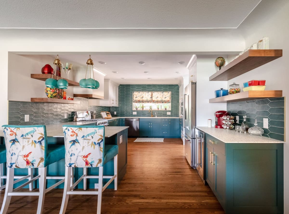 Teal kitchen with floral upholstered stools at the island, walnut floating shelves and teal tile