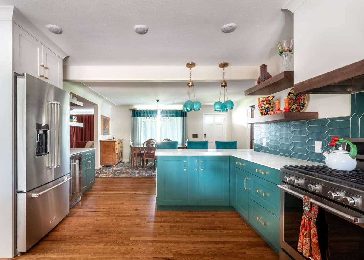 Teal kitchen seen from the refrigerator, with a stainless range, walnut shelves and the dining room beyond