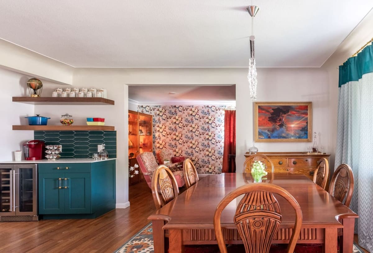 Teal coffee bar with walnut floating shelves beside a dining room with a carved wood table