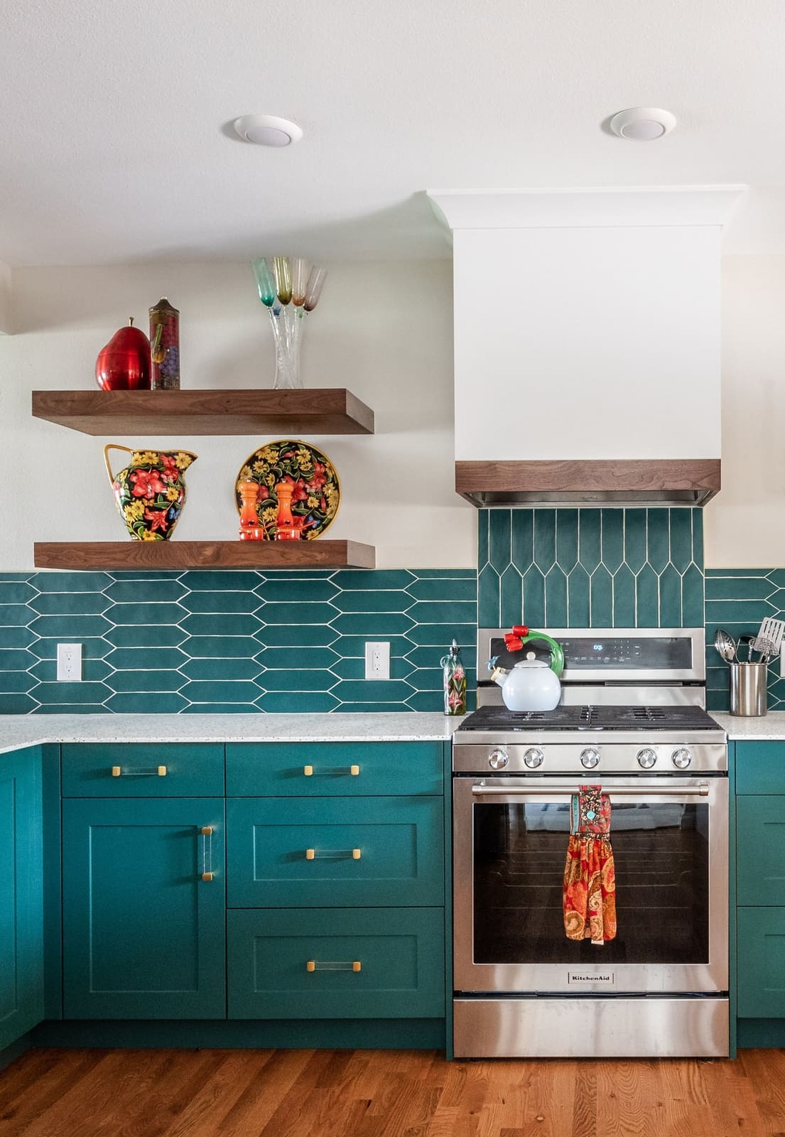 Range wall with a white hood, walnut shelves of red pottery and teal picket tile