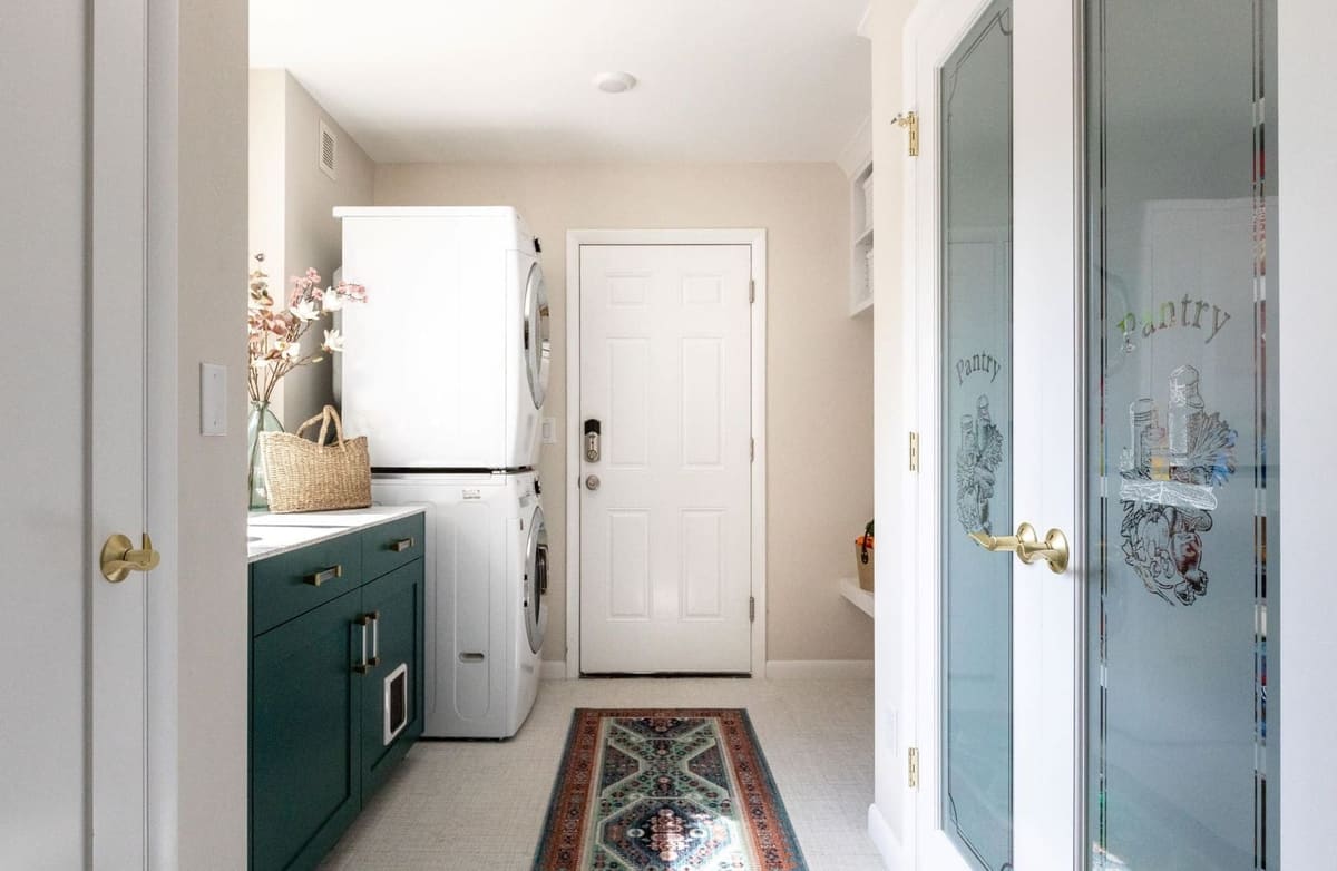 Laundry entry with a stacked washer and dryer, teal cabinet and a pantry door with etched glass