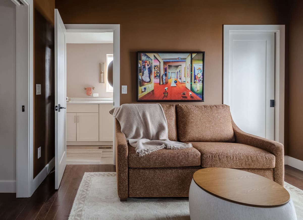 Rust sleeper sofa with a white drum table and colorful framed art, a bath through the open door