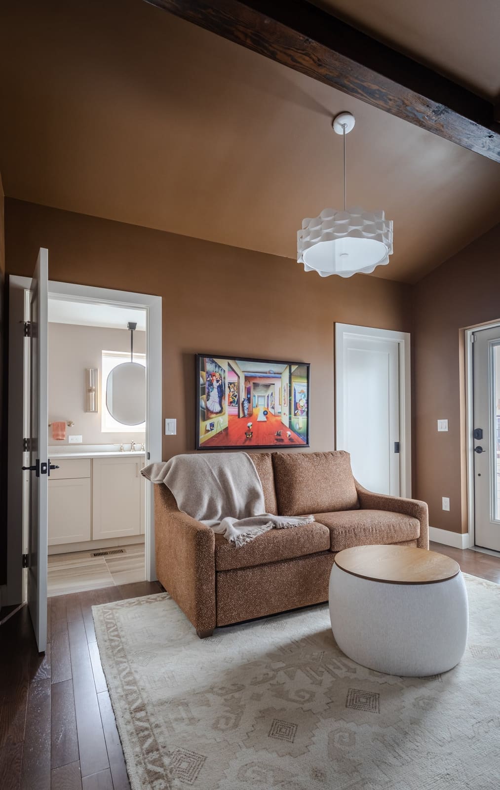Office sitting area with a rust sofa and white drum table under a beamed sloped ceiling