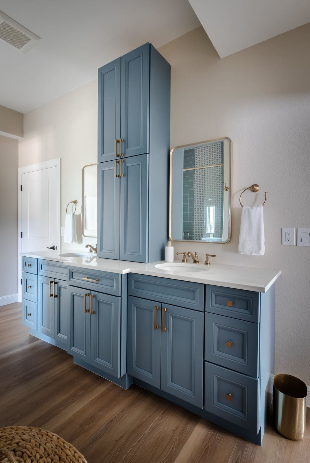 Misty blue double vanity with a center linen tower and brass hardware on wood-look floors