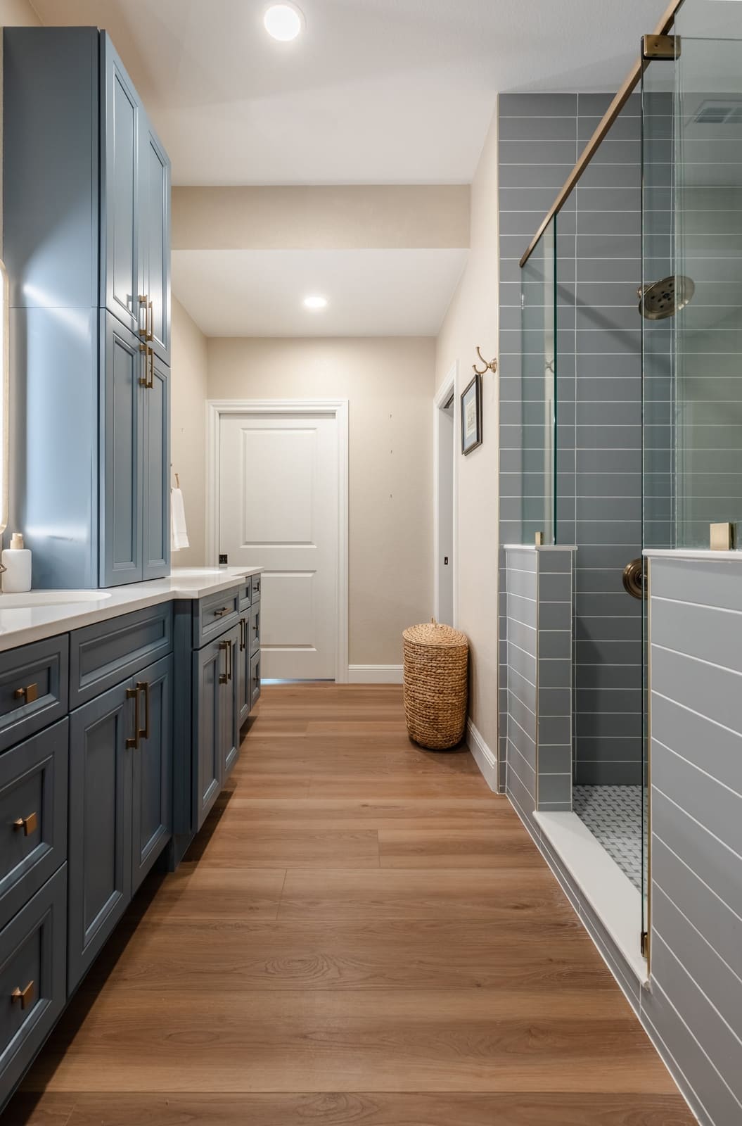 Long bath with a blue vanity on one side and a glass walk-in shower in gray-blue tile on the other