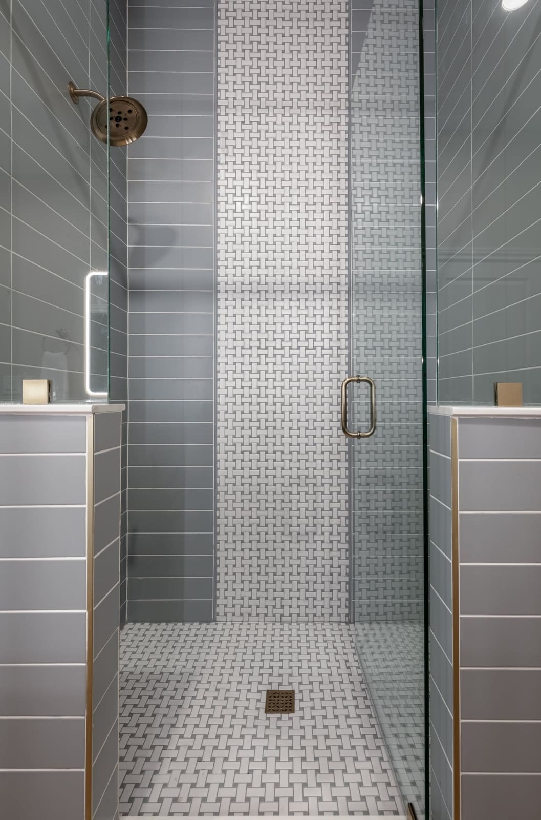 Walk-in shower in gray-blue subway tile with a white mosaic accent stripe and mosaic floor