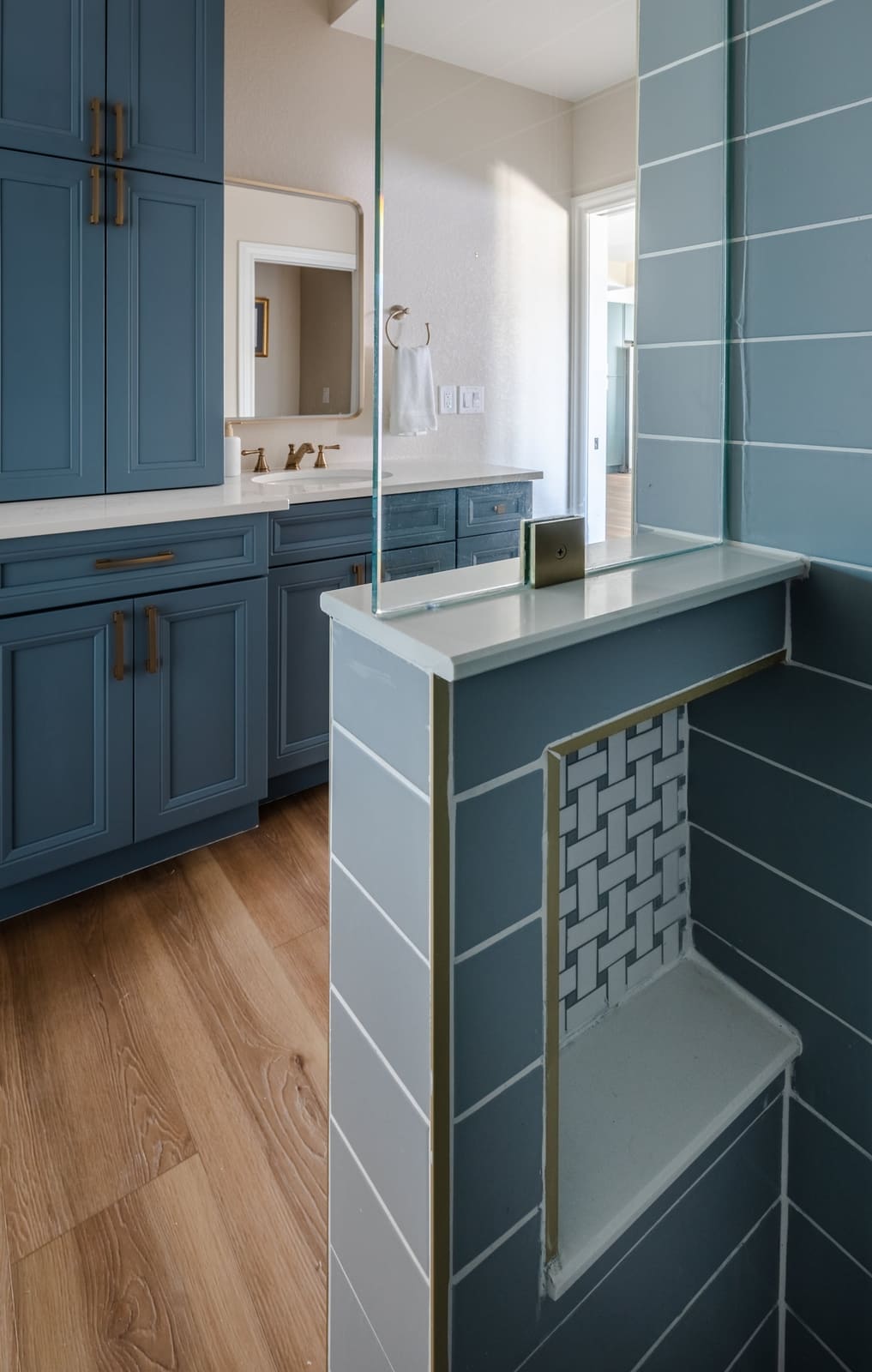 Shower half wall with a tiled niche in gray-blue and white mosaic beside the blue vanity