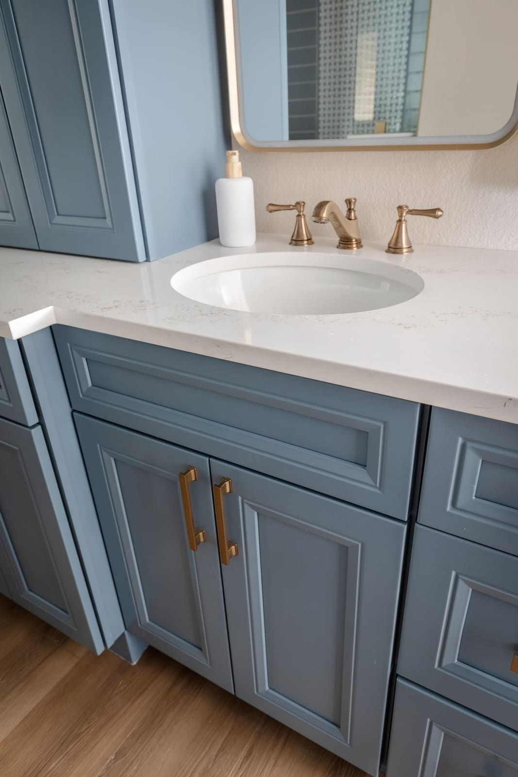 Misty blue raised-panel vanity with brass pulls and a white quartz top