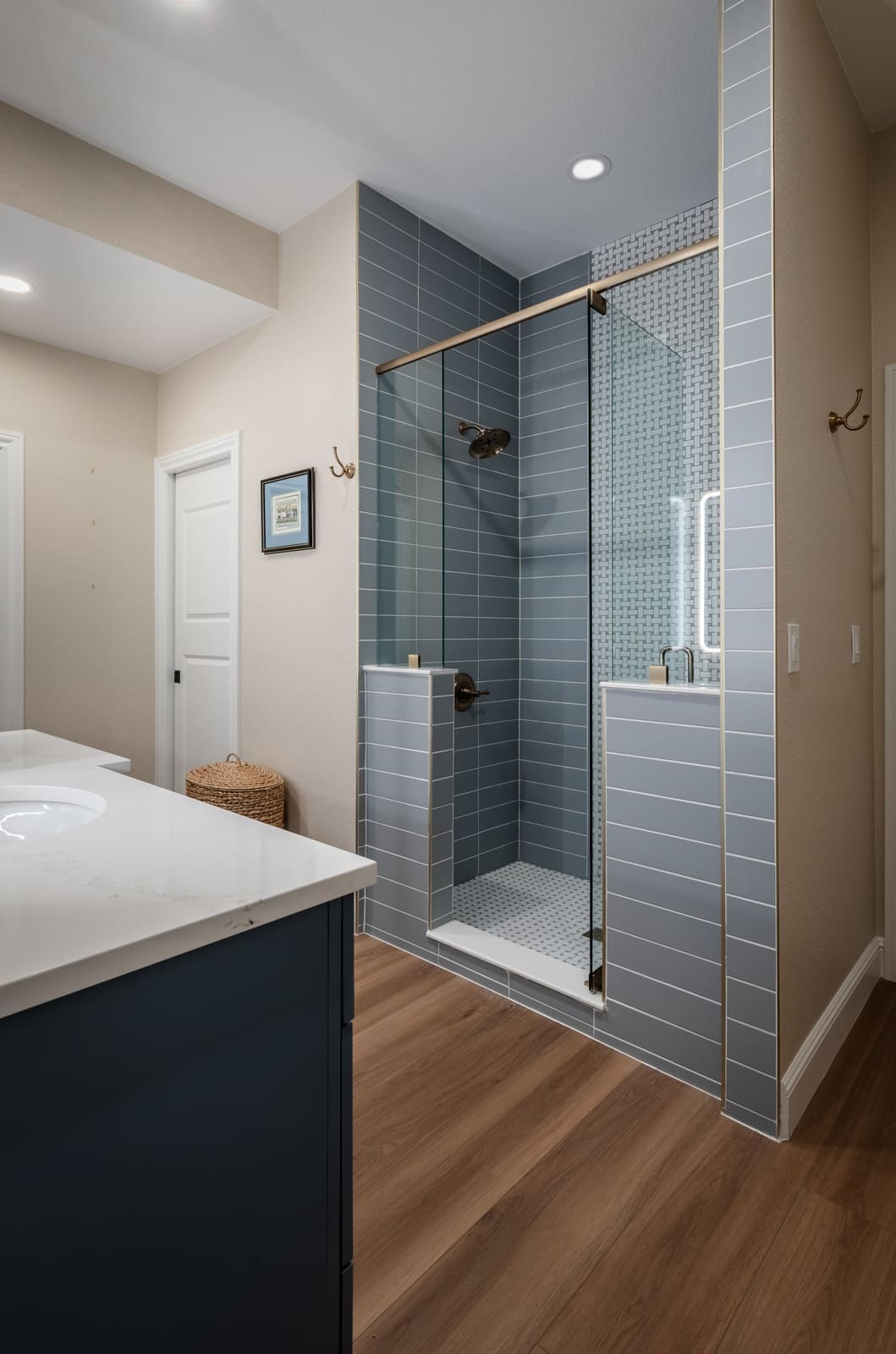 Glass walk-in shower in gray-blue tile seen past the vanity