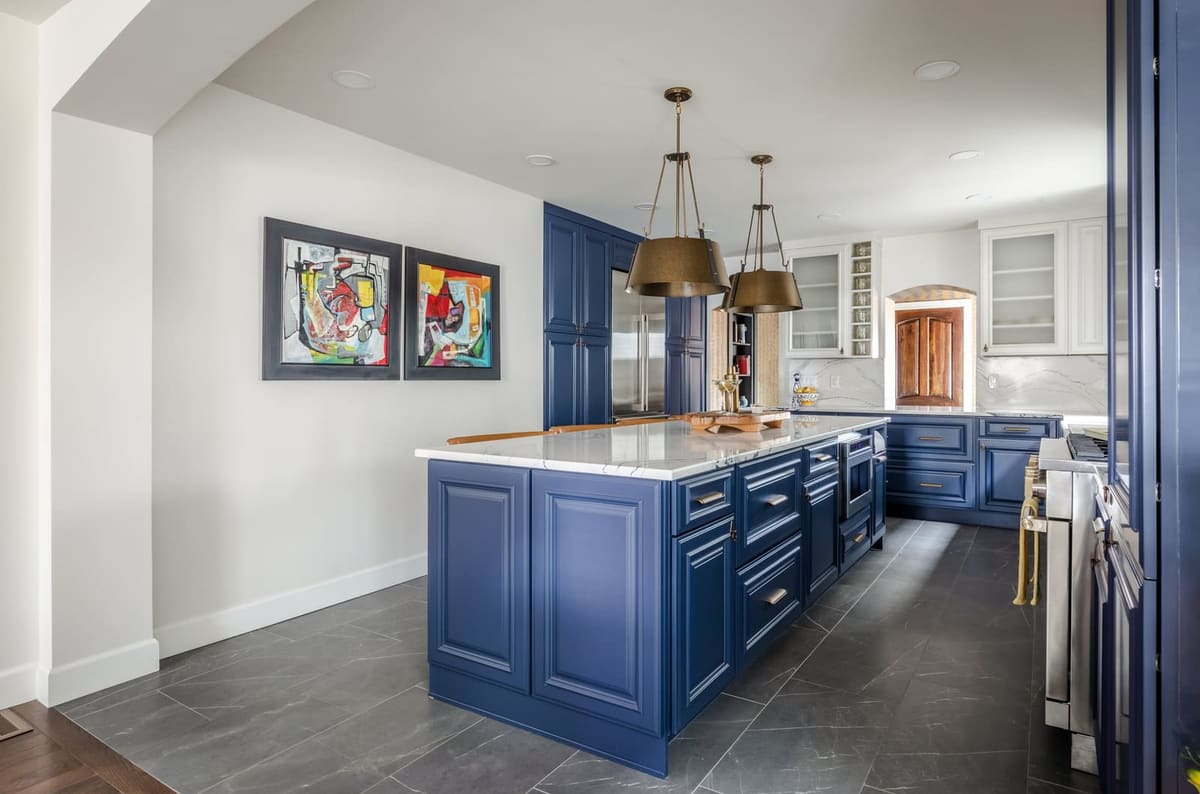 Navy kitchen island under brass dome pendants beside a navy pantry wall and white uppers