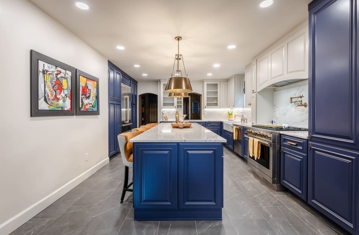 Long view of the navy island and white kitchen over gray stone-look tile floors