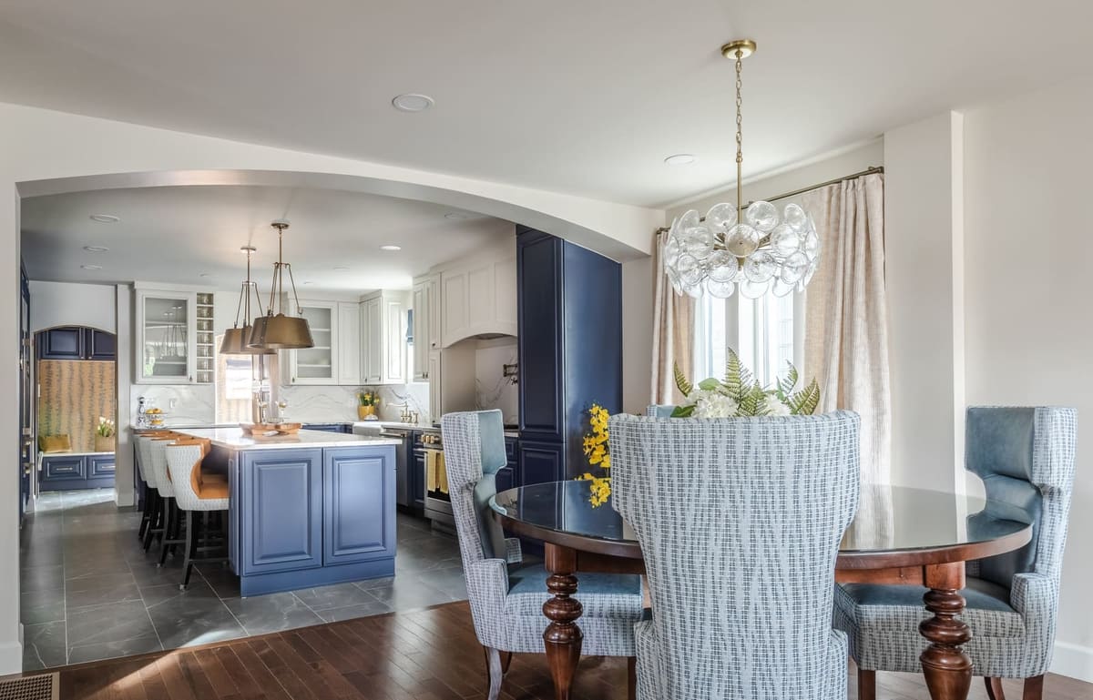 Dining room with a round table and upholstered chairs opening onto the navy kitchen through an arch