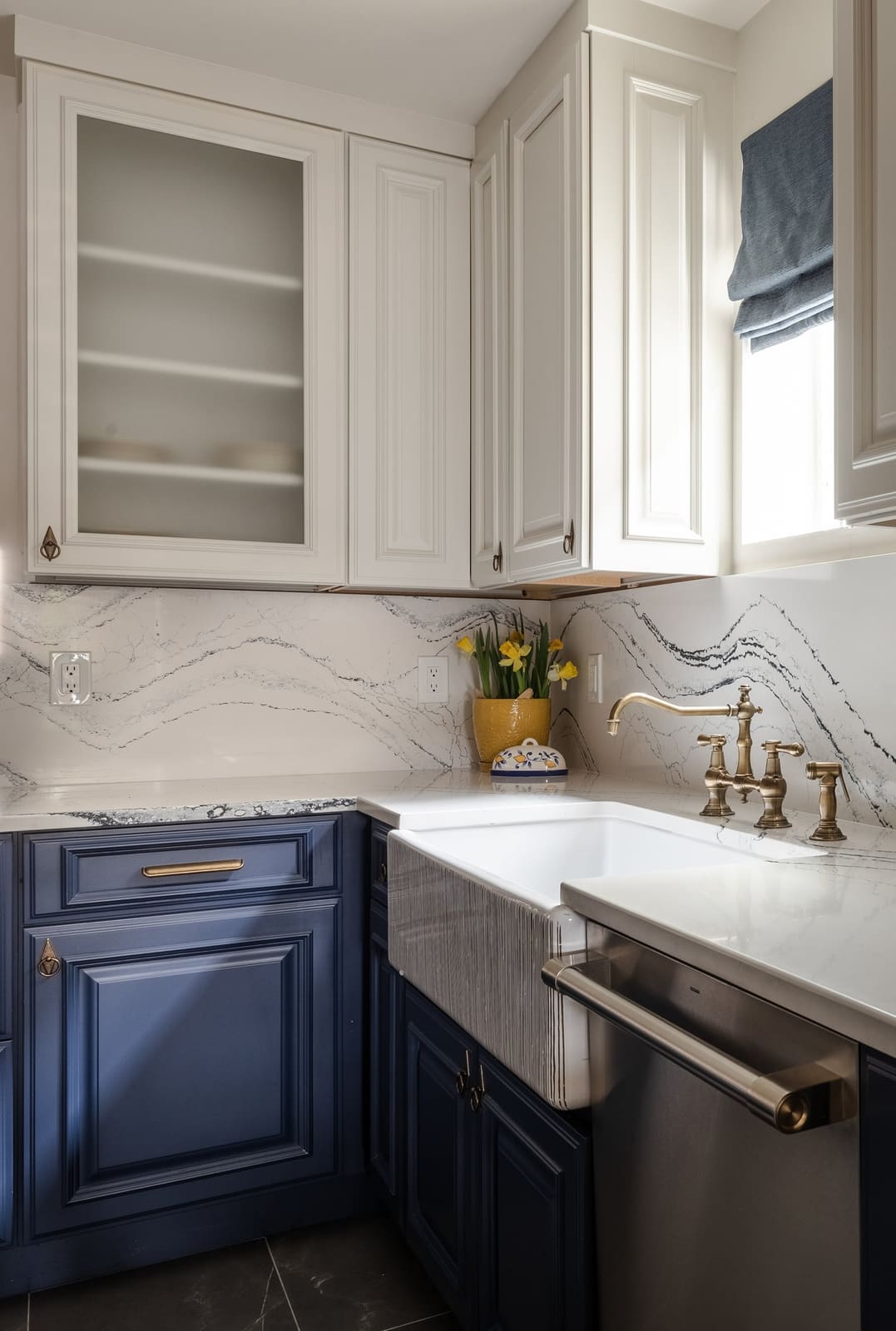 Farmhouse sink with a bridge faucet below white glass-front cabinets