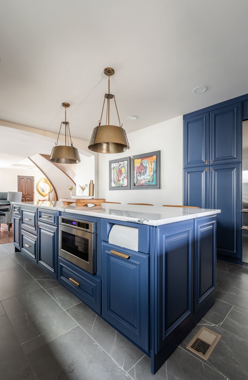 Navy island with a built-in microwave drawer under brass pendants