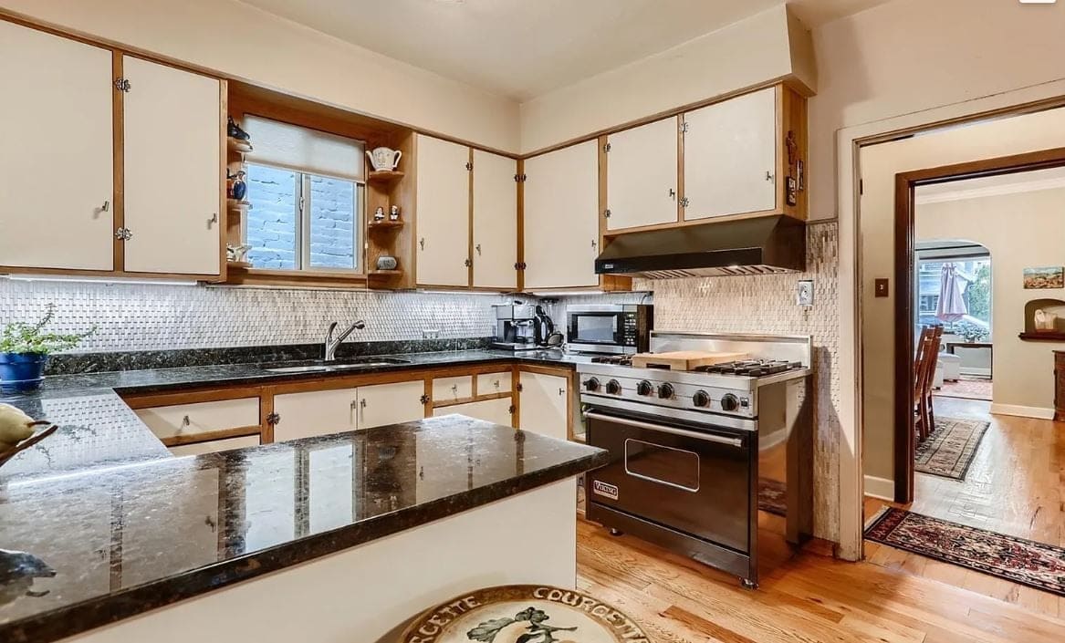 Before the remodel: U-shaped kitchen with cream cabinets, black granite counters and a stainless range