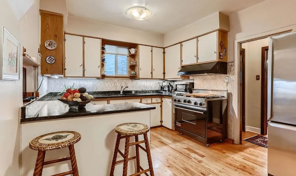 Before the remodel: black granite peninsula with wicker stools facing the old cream and wood cabinets