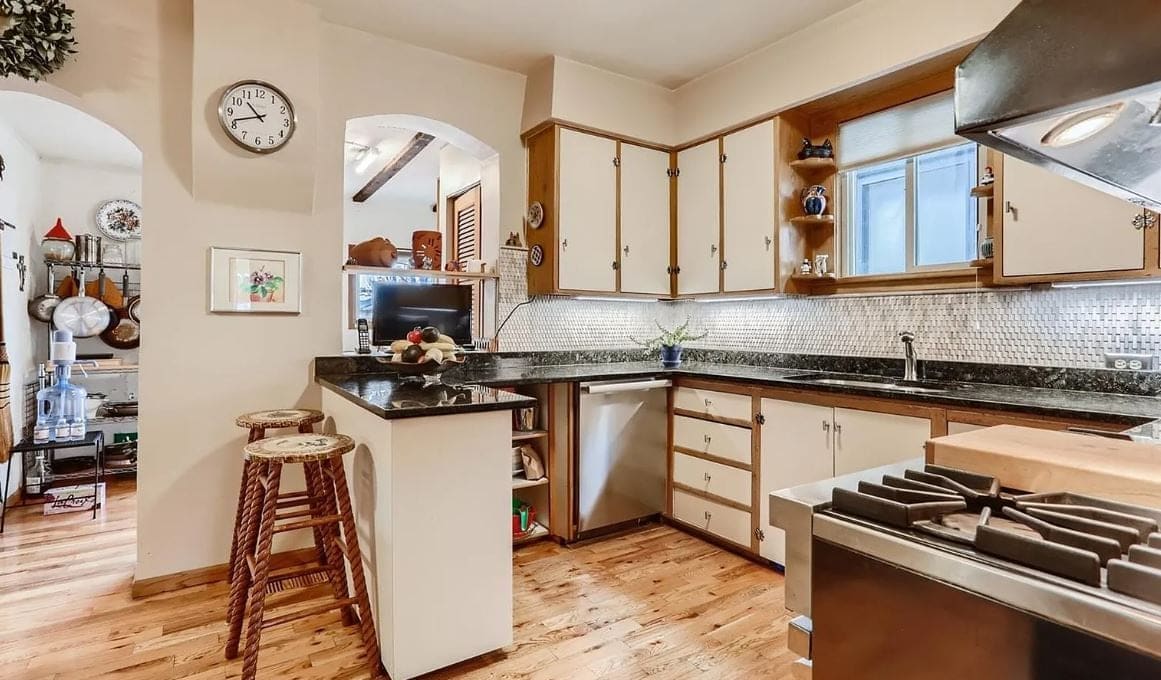 Before the remodel: kitchen corner with a granite peninsula, wood stools and an arched doorway