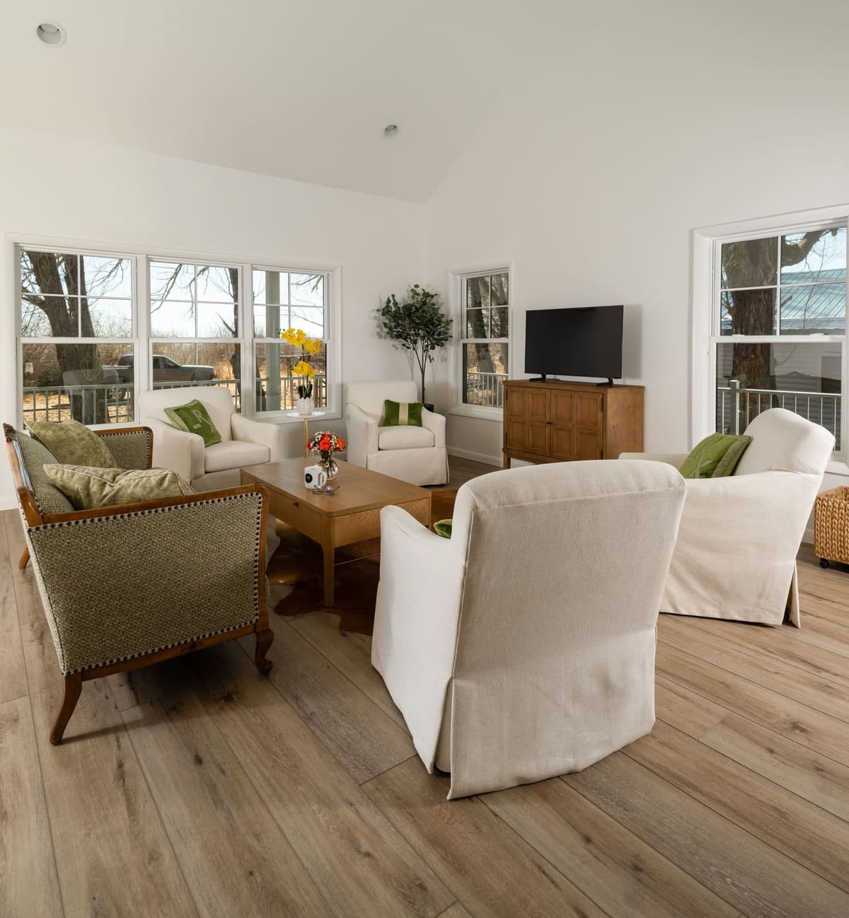 White slipcovered chairs and a wood console under a wall of windows in the living room