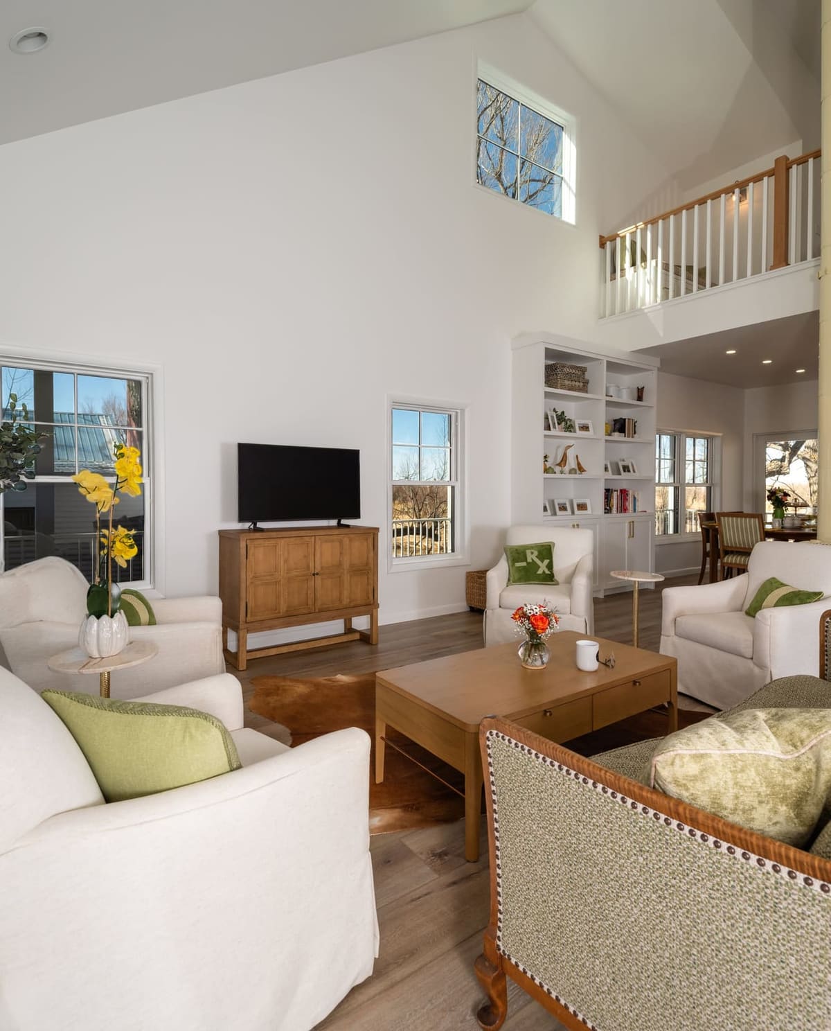 Vaulted living room with white chairs and green pillows around a wood coffee table