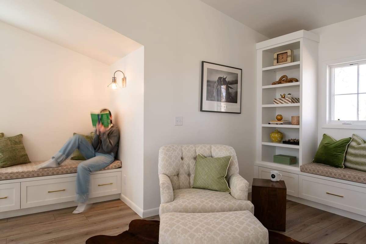 Reading nook with a built-in window bench, white bookshelves and a tufted chaise