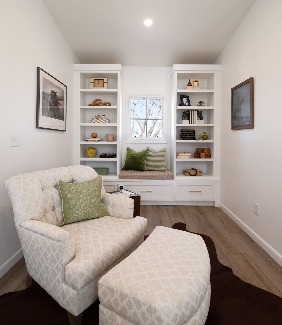 Tufted chair and ottoman facing a window seat framed by built-in white bookshelves