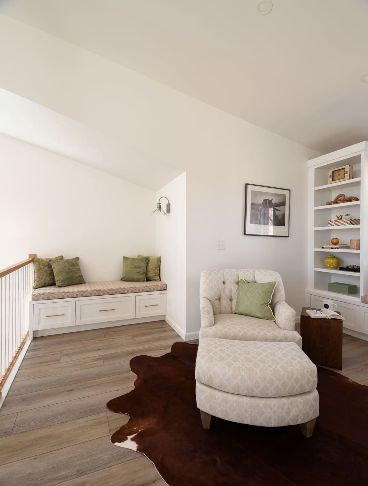 Loft reading corner with a tufted chair and ottoman on a cowhide rug beside built-in shelves