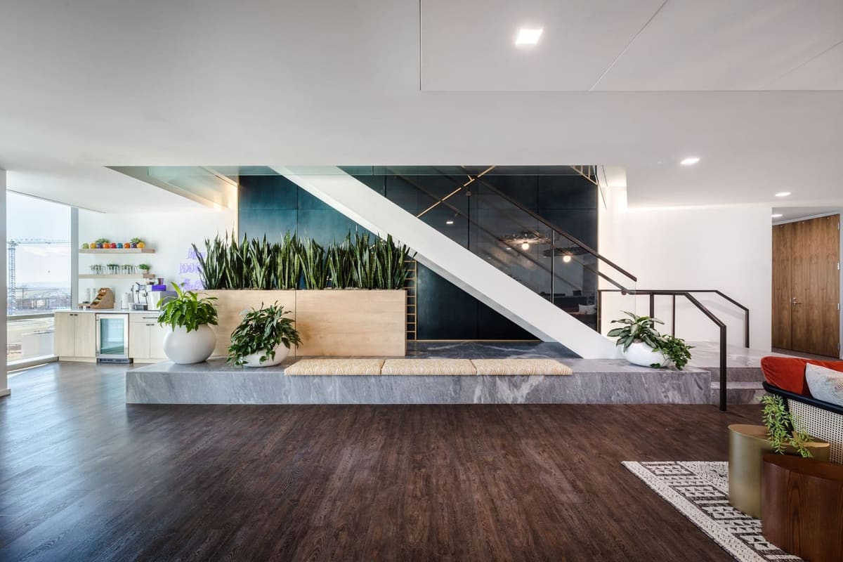 Open office commons with a navy feature stair, a planted stone platform and dark wood floors