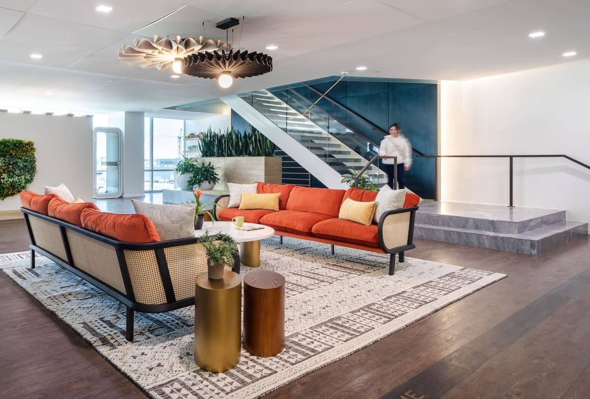Office lounge with orange sofas under a woven pendant, the navy feature stair beyond