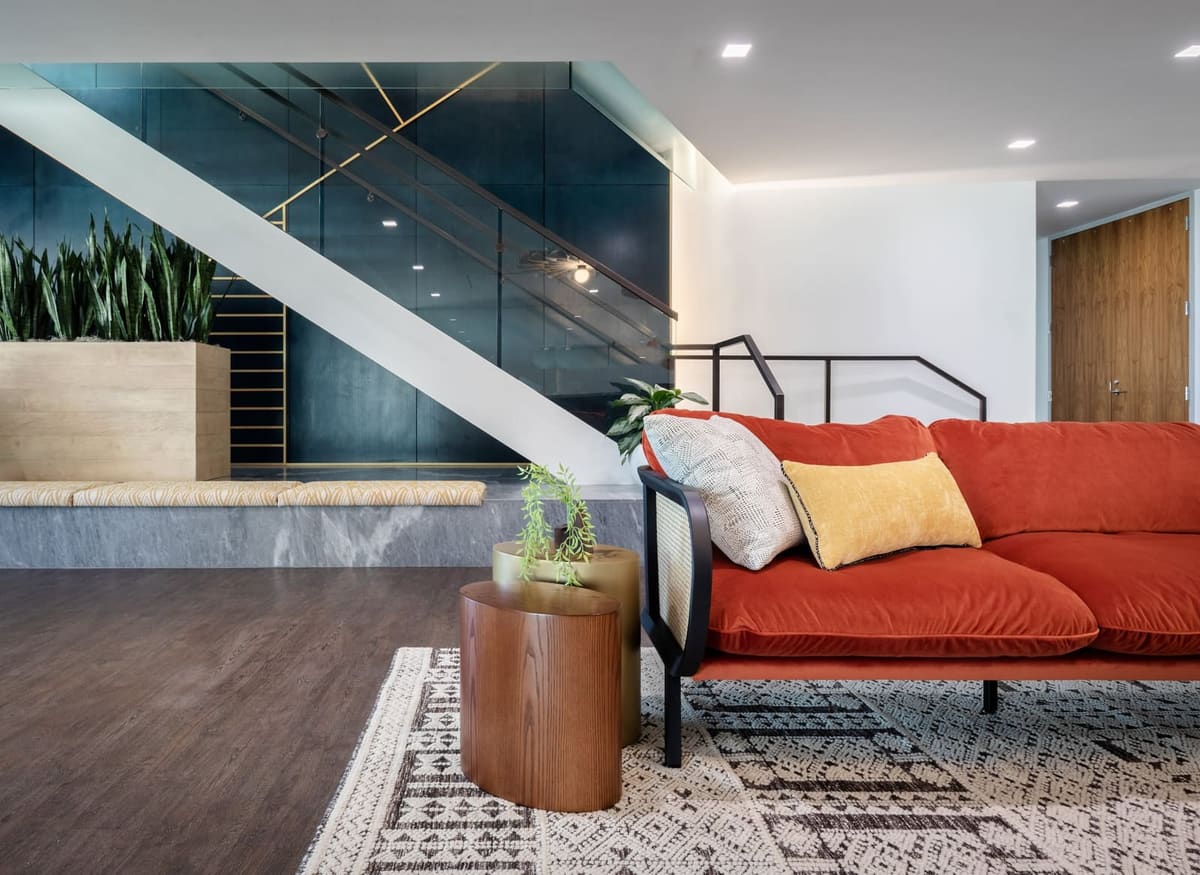 Orange sofa and wood drum table on a patterned rug at the foot of the navy feature stair