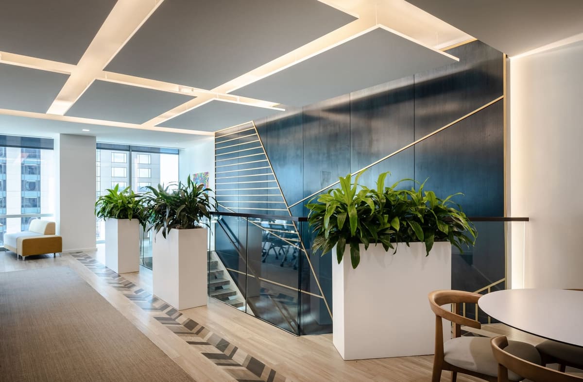 Stair landing with a navy wall inlaid with brass lines, white planters and an angled skylight ceiling