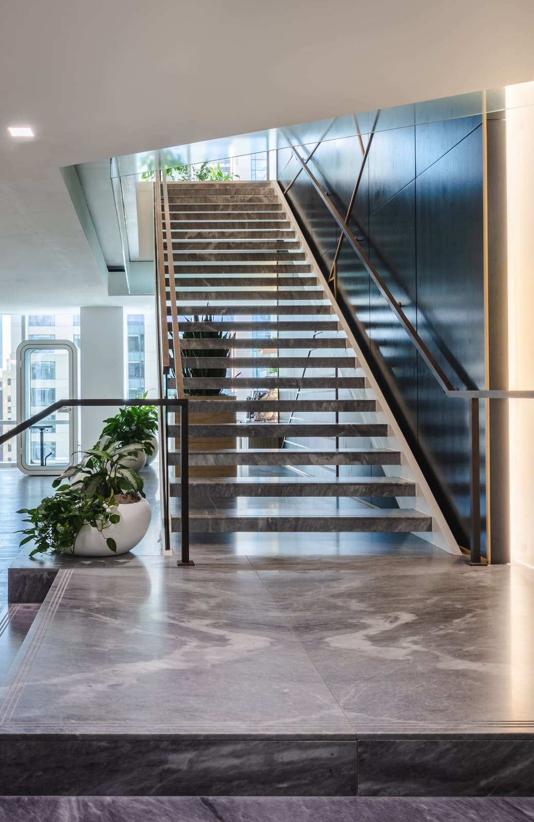 Floating office stair with glass rails rising against a navy wall