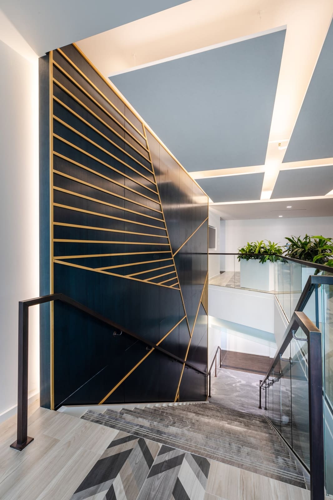 Navy stair wall inlaid with diagonal brass lines below a sculpted ceiling