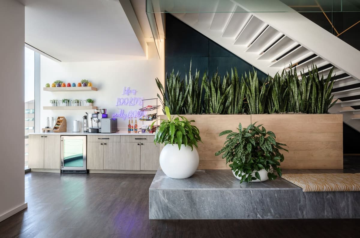 Office kitchenette with oak cabinets beside a planted stone platform under the feature stair