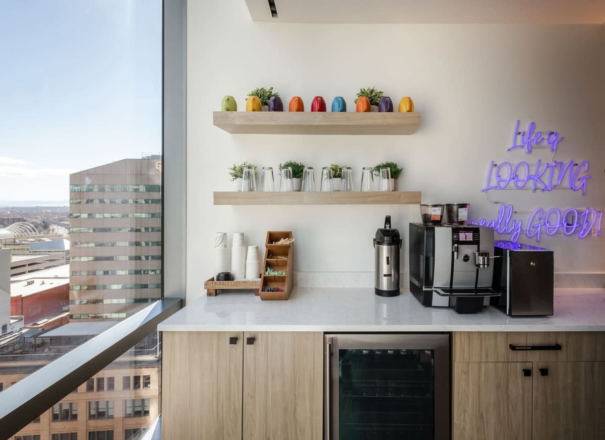 Coffee bar with oak cabinets, floating shelves of colorful mugs and a purple neon sign