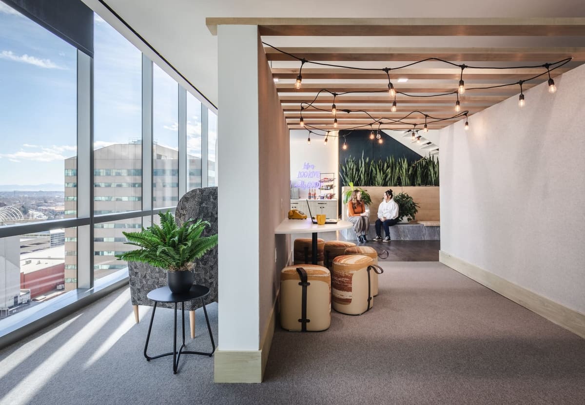 Café nook under a slatted wood ceiling with string lights, upholstered stools and city views