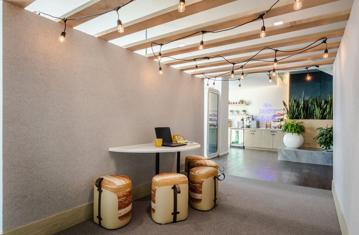 Café table and upholstered wood stools under a slatted ceiling strung with lights