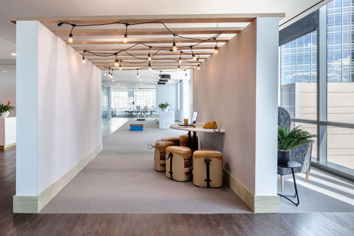 Long café nook with string lights and wood stools looking across the open office floor
