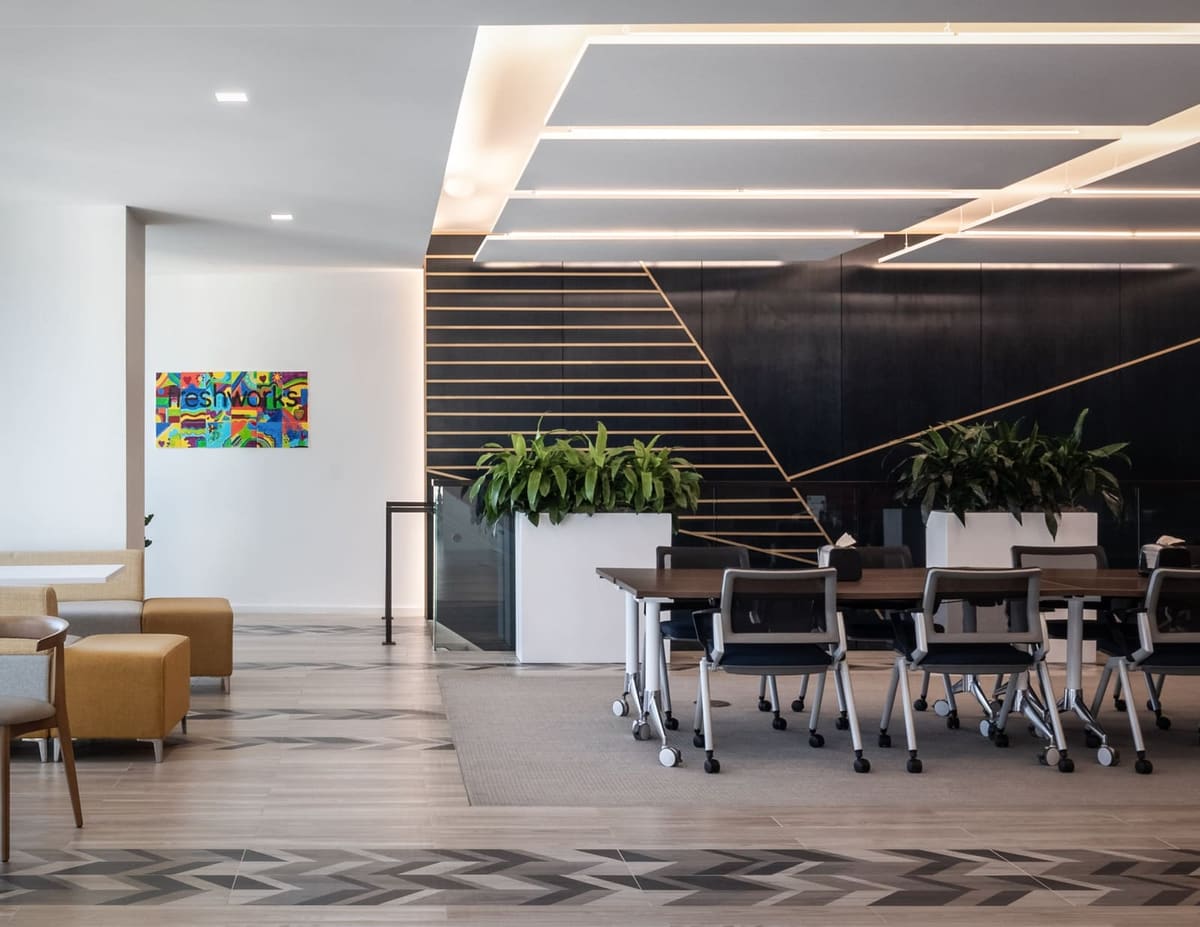 Training room with rows of tables and black chairs below a navy stair wall with brass lines