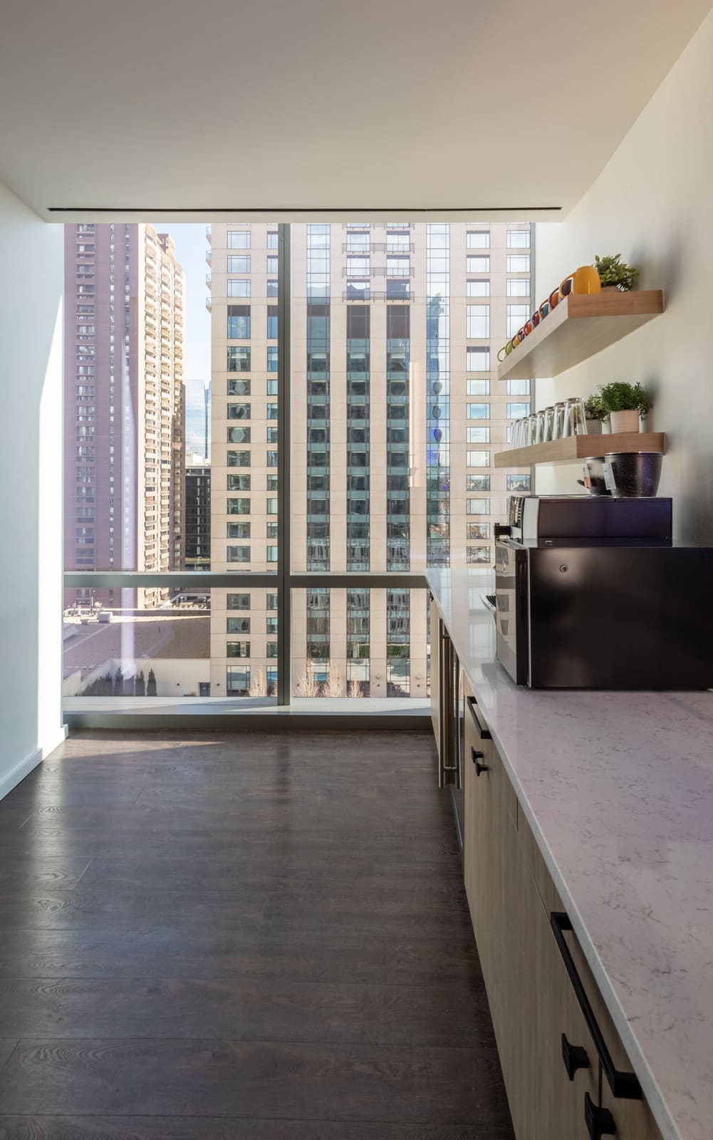 Office kitchenette corridor with tall windows framing downtown towers