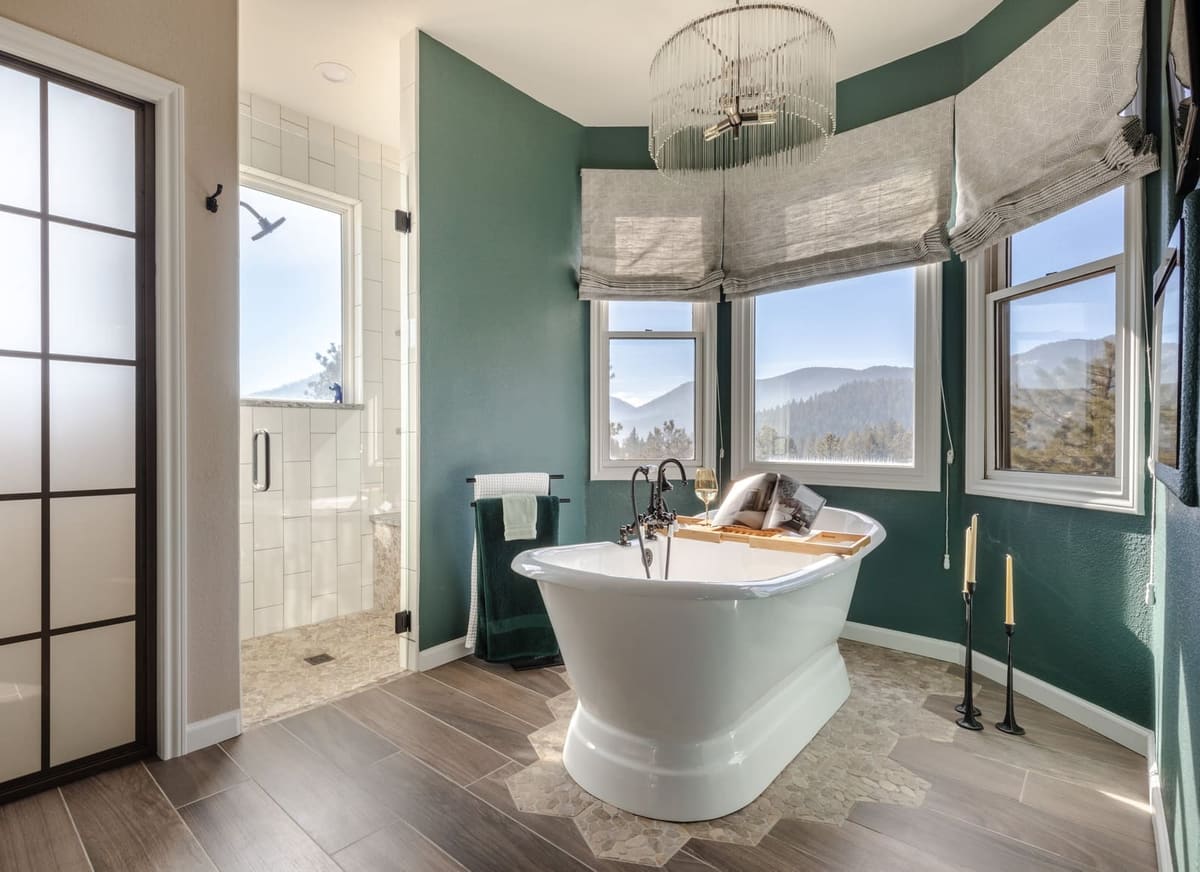 Freestanding tub framed by green walls and mountain views, a frosted glass door to the shower