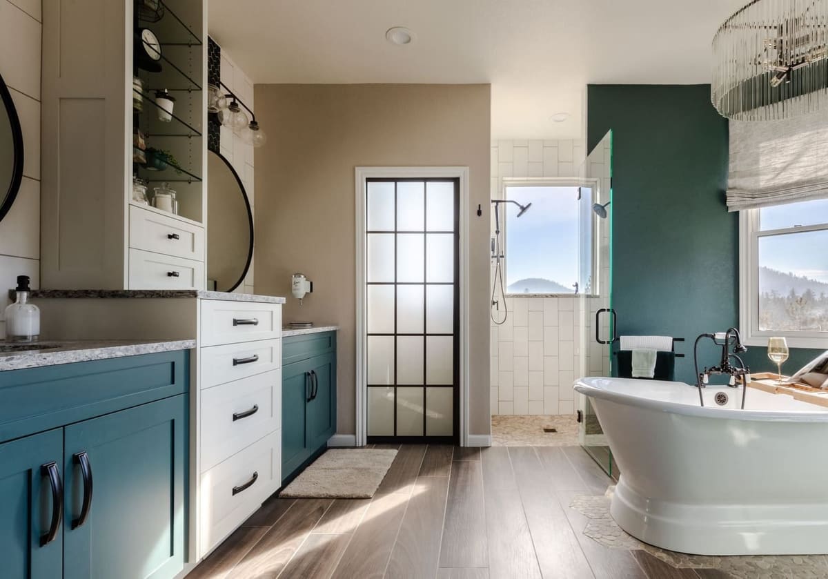 Primary bath with teal and white cabinets leading to a freestanding tub in a green bay window