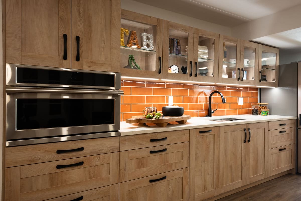 Kitchenette wall with a built-in oven, glass-front oak uppers, orange subway tile and a matte black faucet