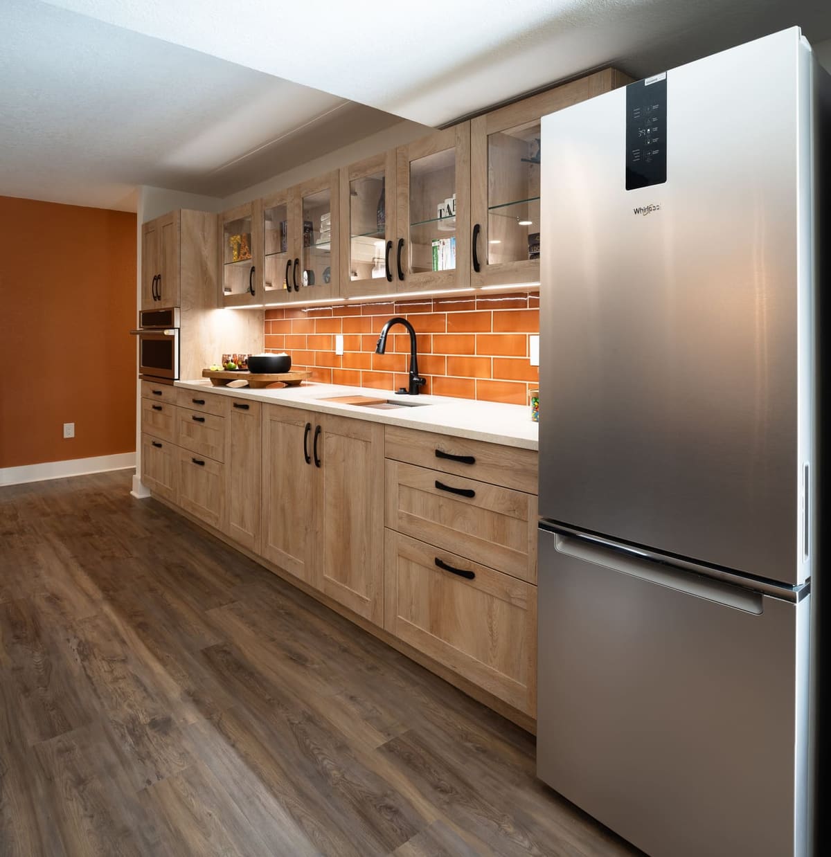 Basement kitchenette with a stainless refrigerator, oak shaker cabinets and an orange accent wall
