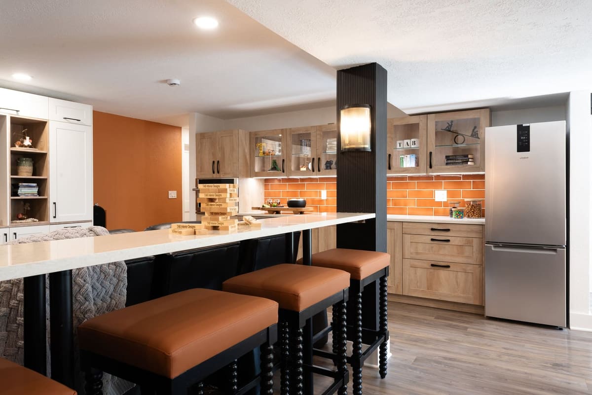 Basement peninsula with cognac leather stools on black spindle legs beside a fluted black column and sconce