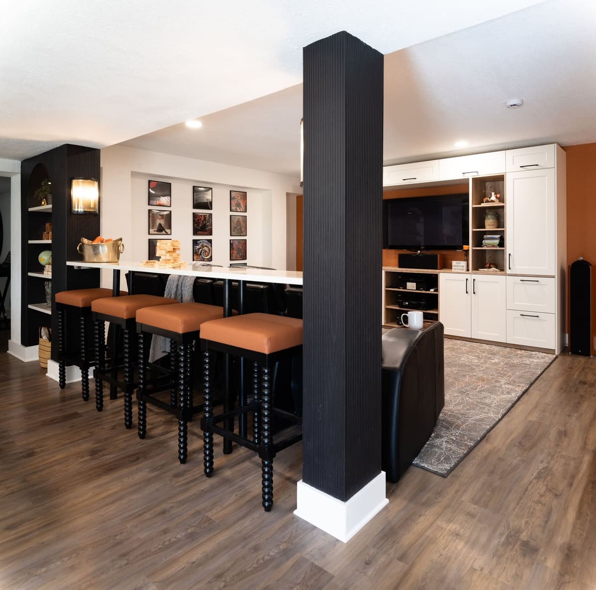 Basement bar counter with four cognac leather stools and a fluted black column, media built-ins beyond